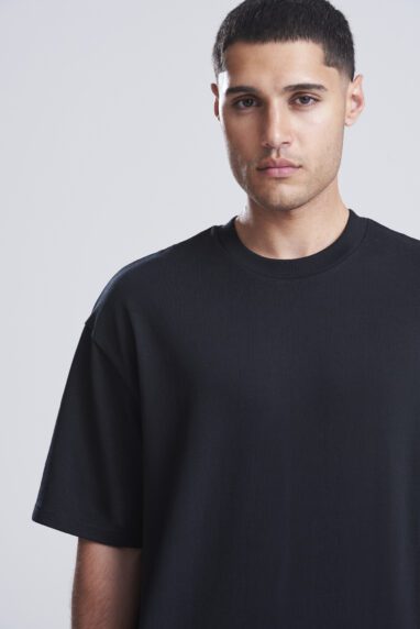 Man with short dark hair wearing a plain black T-shirt, facing the camera with a neutral expression.