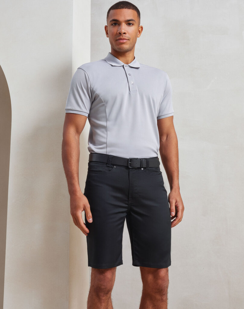 Man standing in a neutral studio wearing a light gray polo shirt and black shorts, facing the camera.