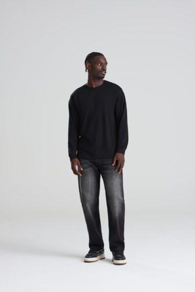 AT012_DEEP_BLACK_DEC2025-DEC2027_012-382x572 - Topline Workwear Man in a black long-sleeve shirt, faded jeans, and black-and-white sneakers stands in a photo studio with a light gray background.