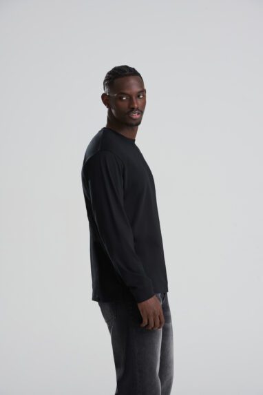 AT012_DEEP_BLACK_DEC2025-DEC2027_047-382x572 - Topline Workwear Man in a black long-sleeve shirt standing in profile, looking over his shoulder against a light gray studio backdrop.