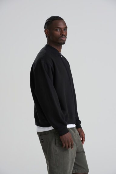 JH124_DEEP_BLACK_DEC2025-DEC2027_152-382x572 - Topline Workwear Man in a black sweatshirt over a white tee, with gray shorts, standing in profile against a light studio background.