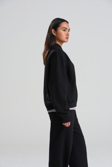 JH124_DEEP_BLACK_DEC2025-DEC2027_459-382x572 - Topline Workwear Side profile of a woman with long dark hair, dressed in a black sweater and black wide-leg pants, standing against a light gray studio background.